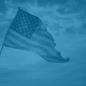 Wide angle photo of a tattered American flag blowing in the wind against a beautiful cloudscape